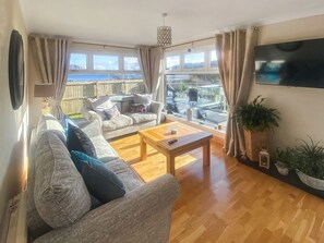 Sala de estar com sofá, mesa de centro, televisão e vista para o exterior.