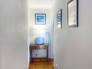 A narrow hallway with a wooden console table, a lamp, and framed artwork on the walls. - 3 bedroom accommodation in Lamlash (Lamlash)