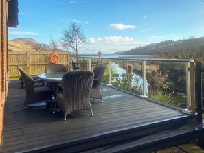 Una terraza con mobiliario de mimbre y barandilla de cristal con vistas a un río.