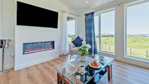 Una sala de estar moderna con chimenea, una mesa de centro de vidrio y un ventanal con vistas al campo.