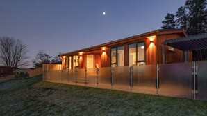 Una casa moderna con porche cubierto, ventanas grandes y una luna en el cielo.