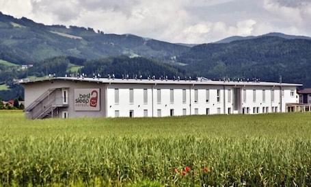 A hotel with a sign reading "Best Sleep Hotel" in a rural setting with a field in the foreground and mountains in the background.. ART HOTEL SPIELBERG