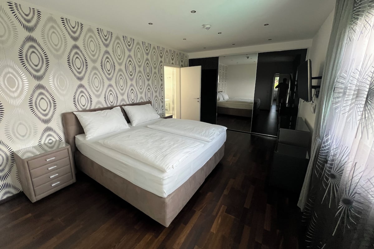 Une chambre moderne avec un grand lit, une table de chevet, une armoire et un miroir.