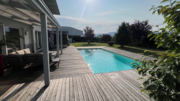 Una terraza de madera con piscina, un área de estar techada y vistas a las montañas.