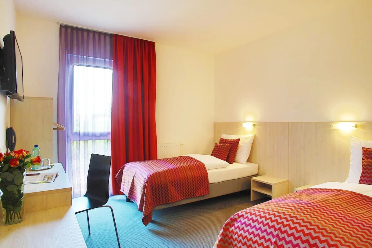 Une chambre d’hôtel comprenant un lit, des tables de chevet, un bureau avec une chaise, une télévision et une fenêtre avec des rideaux.