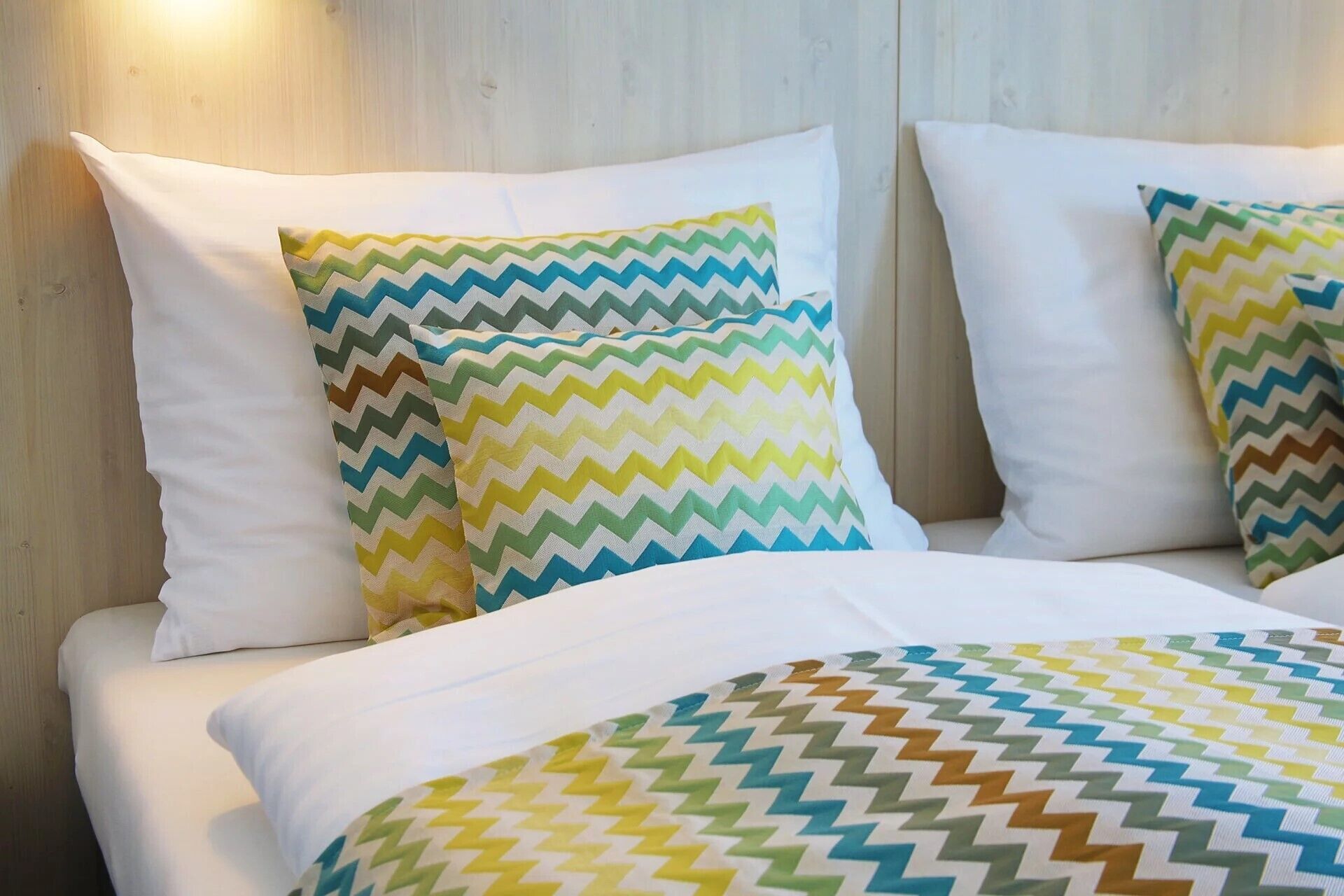 A bed with two pillows featuring a zigzag pattern in multiple colors, a white bedspread, and a wooden headboard.