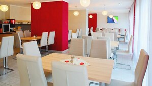 Un restaurante moderno con sillas y mesas blancas, paredes de acento rojas y lámparas esféricas colgantes.