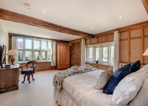 A bedroom with a large bed, wooden beams, a desk, and a chair.