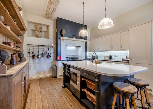 A modern kitchen with wooden cabinetry, a large island, hanging pots, and a stone sculpture.