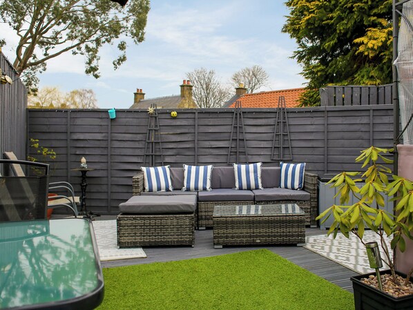 Un espace patio aménagé avec un ensemble de canapés, du gazon synthétique et une plante en pot.