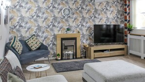 A living room with a sofa, ottoman, TV, fireplace, and tropical wallpaper.