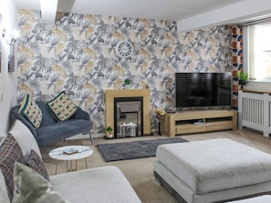 Una sala de estar con sofá, reposapiés, televisor, chimenea y papel tapiz tropical.