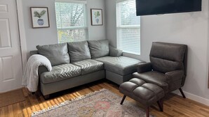 A modern living room with a grey sectional sofa, a brown armchair, and a flat-screen TV mounted on the wall. - Charming 1-bedroom Guesthouse in Central Austin (Austin)