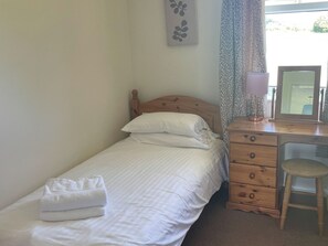 Un lit simple avec une literie blanche, une tête de lit en bois, une table de chevet avec une lampe, un miroir et une chaise.