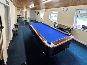 Een pooltafel met een blauwe viltbekleding, een dartbord en een klok aan de muur.