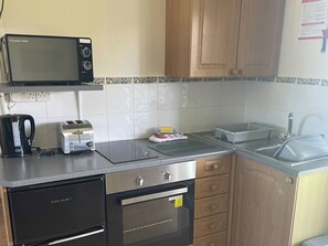 A compact kitchen with a microwave, toaster, kettle, and a dishwasher.