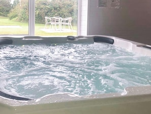 Un bain à remous avec vue sur une zone verdoyante et une chaise blanche installée à l’extérieur.