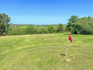 A golf course with a red flag, green grass, trees, and distant buildings.
