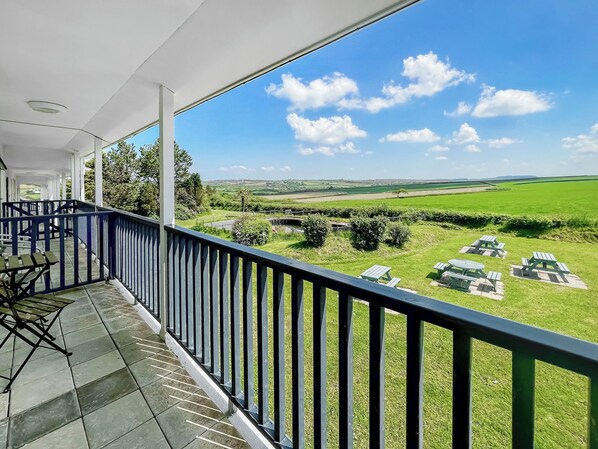 A balcony with a view of a green landscape and picnic tables.