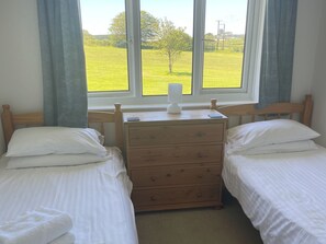 Een slaapkamer met twee eenpersoonsbedden, een houten dressoir, een bedlampje en een raam met uitzicht op een groen veld.