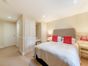 Une chambre à coucher avec un lit, deux tables de chevet, une lampe rouge, une porte blanche et un placard.
