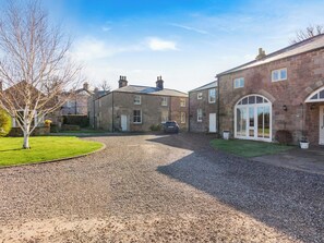 A residential area with stone buildings, a gravel driveway, and a tree.