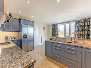A modern kitchen with a stainless steel refrigerator, a built-in water dispenser, a toaster, and a window with floral curtains.