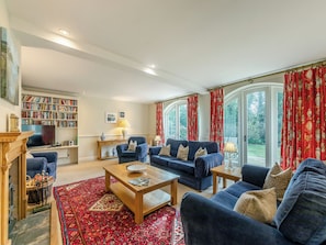 A spacious living room with a large bookshelf, a fireplace, and a view through large windows. - Carriage House - UK49288 (Doxford, near Embleton)