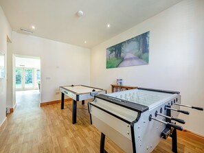 A room with two foosball tables, a painting of a forest path, and a door leading to a balcony.