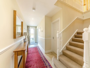 A hallway with a wooden bench, a red patterned rug, a white door, and a staircase with beige carpeted steps.