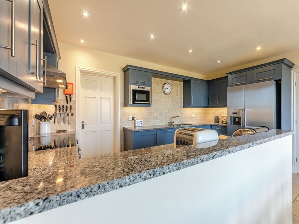 A modern kitchen with granite countertops, stainless steel appliances, and blue cabinetry.