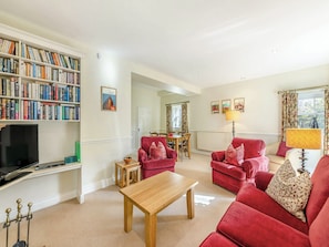 A living room with a bookshelf, red sofas, a wooden coffee table, and a dining area in the background.