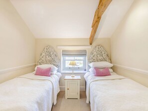 A bedroom with two single beds, a window with a lamp, and a wooden ceiling beam.