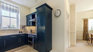 A modern kitchen with dark cabinetry, a built-in oven, and a window with decorative items. - 2 bedroom accommodation in Doxford, near Embleton (Doxford, near Embleton)