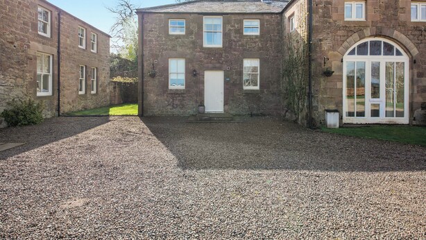A stone building with a gravel driveway, a white door, and a large arched window. - 2 bedroom accommodation in Doxford, near Embleton (Doxford, near Embleton)