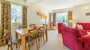 A living room with a wooden dining table, red sofas, and floral curtains. - 2 bedroom accommodation in Doxford, near Embleton (Doxford, near Embleton)