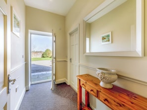 A hallway with a door leading outside, a wooden console table, and a framed picture on the wall.