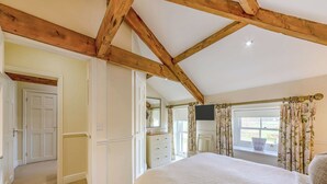 A bedroom with a large bed, wooden ceiling beams, a television, and a window with curtains. - 2 bedroom accommodation in Doxford, near Embleton (Doxford, near Embleton)