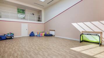 A spacious room with a high ceiling, a balcony, a children's play area, and a sports goal.
