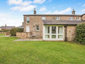 A stone house with a small patio, a white door, and a window with curtains.