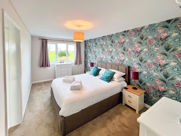 A bedroom with a bed, nightstands, a lamp, a dresser, and a window with curtains.