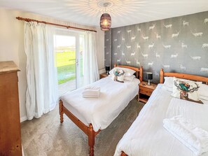Une chambre avec deux lits, une fenêtre avec des rideaux, un mur à motifs et un luminaire au plafond.