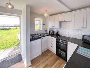 A modern kitchen with white cabinets, a black countertop, a built-in oven, and a window overlooking a green outdoor area.
