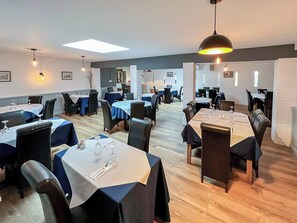 Een restaurant met meerdere tafels, stoelen en hanglampen.