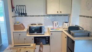A compact kitchen with a microwave, toaster, kettle, and sink. - Goldfinch Apartment - UK49296 (Woolfardisworthy, Clovelly)