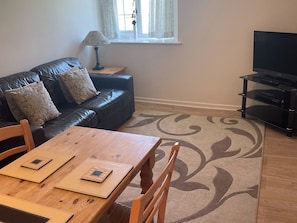 A living room with a leather sofa, a wooden coffee table, a TV stand, and a patterned rug.