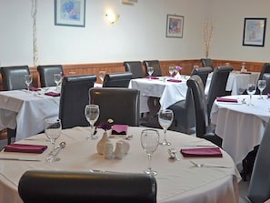 A restaurant with round tables, black leather chairs, white tablecloths, and framed artwork on the walls.