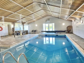 An indoor swimming pool with a tiled floor, a wooden ceiling, and a seating area with chairs.