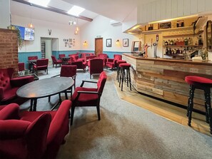 A bar area with a wooden counter and stools, surrounded by red upholstered chairs and tables. - Goldfinch Apartment - UK49296 (Woolfardisworthy, Clovelly)
