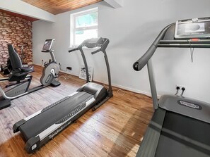 A home gym with treadmills and exercise bikes, wooden flooring, a stone wall, and a window.
